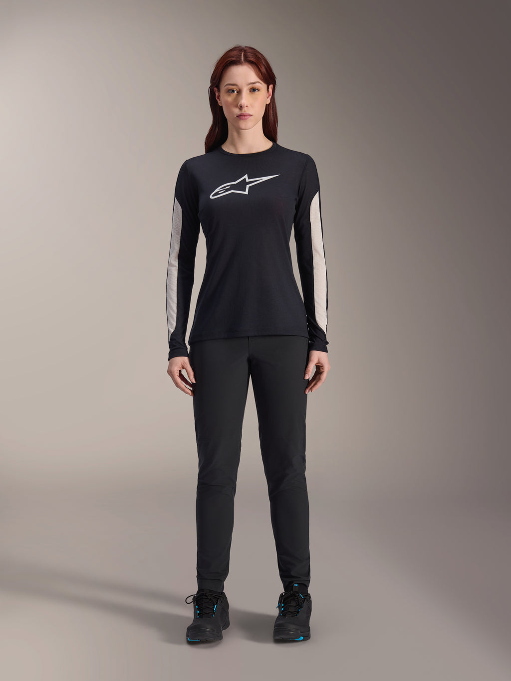 Woman wearing Alpinestars Stella A-Dura Dri Astar Long Sleeve Jersey, Black with white chest logo and light-colored mesh sleeve panels, paired with black pants and black shoes, technical mountain bike apparel