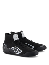 Alpinestars Supertech Shoes, Auto Racing Shoes, Black, featuring a fully knitted fire-retardant upper and carbon fiber heel cup, white Alpinestars logo on the side, FIA/SFI certification labels on the tongue, professional motorsport footwear with a sleek design