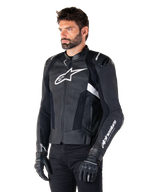 Alpinestars Missile V3 Leather Jacket, Black and White, worn by a man with black riding gloves, featuring a prominent white Alpinestars logo on the chest, external shoulder sliders, and perforated panels for a racing-inspired look.
