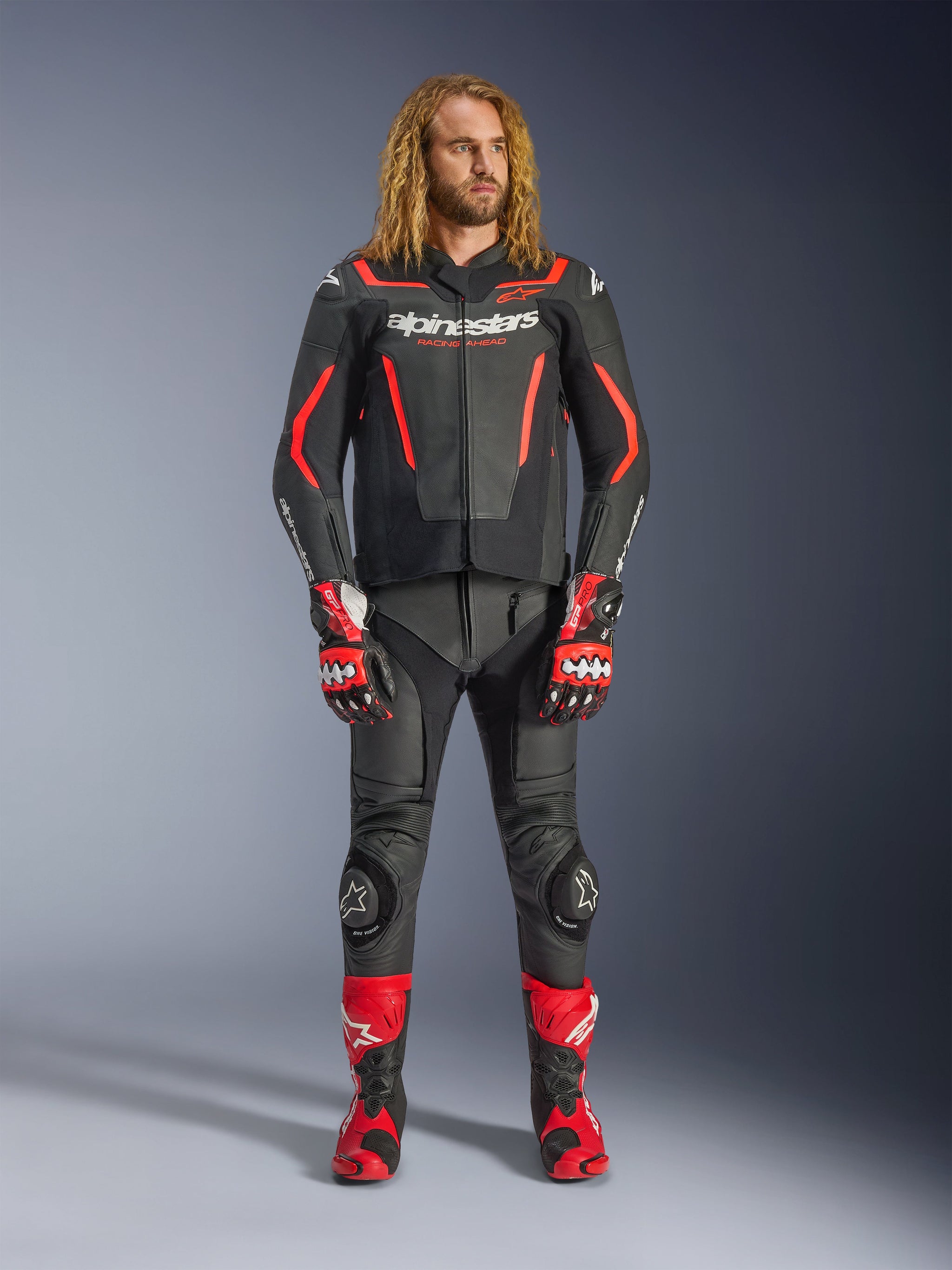 Male model wearing the Alpinestars GP Force V2 Leather Jacket in Black and Red Fluo, paired with matching leather pants, red racing gloves, and red performance boots, professional motorcycle sport gear