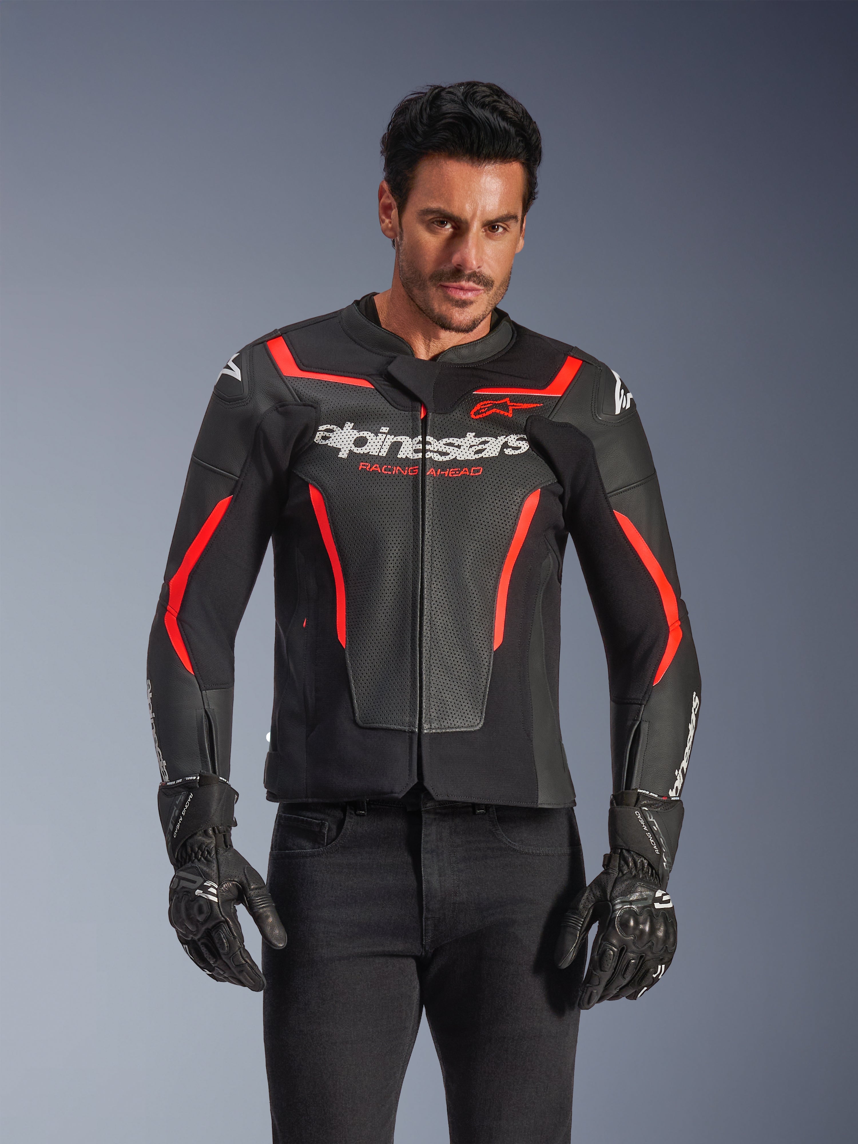 Alpinestars GP Force V2 Air Leather Jacket, Motorcycle Racing Jacket, Black and Red Fluo, premium leather construction with extensive perforations for airflow, worn by a model with black gloves and pants, featuring bold branding and 'Racing Ahead' text on the chest