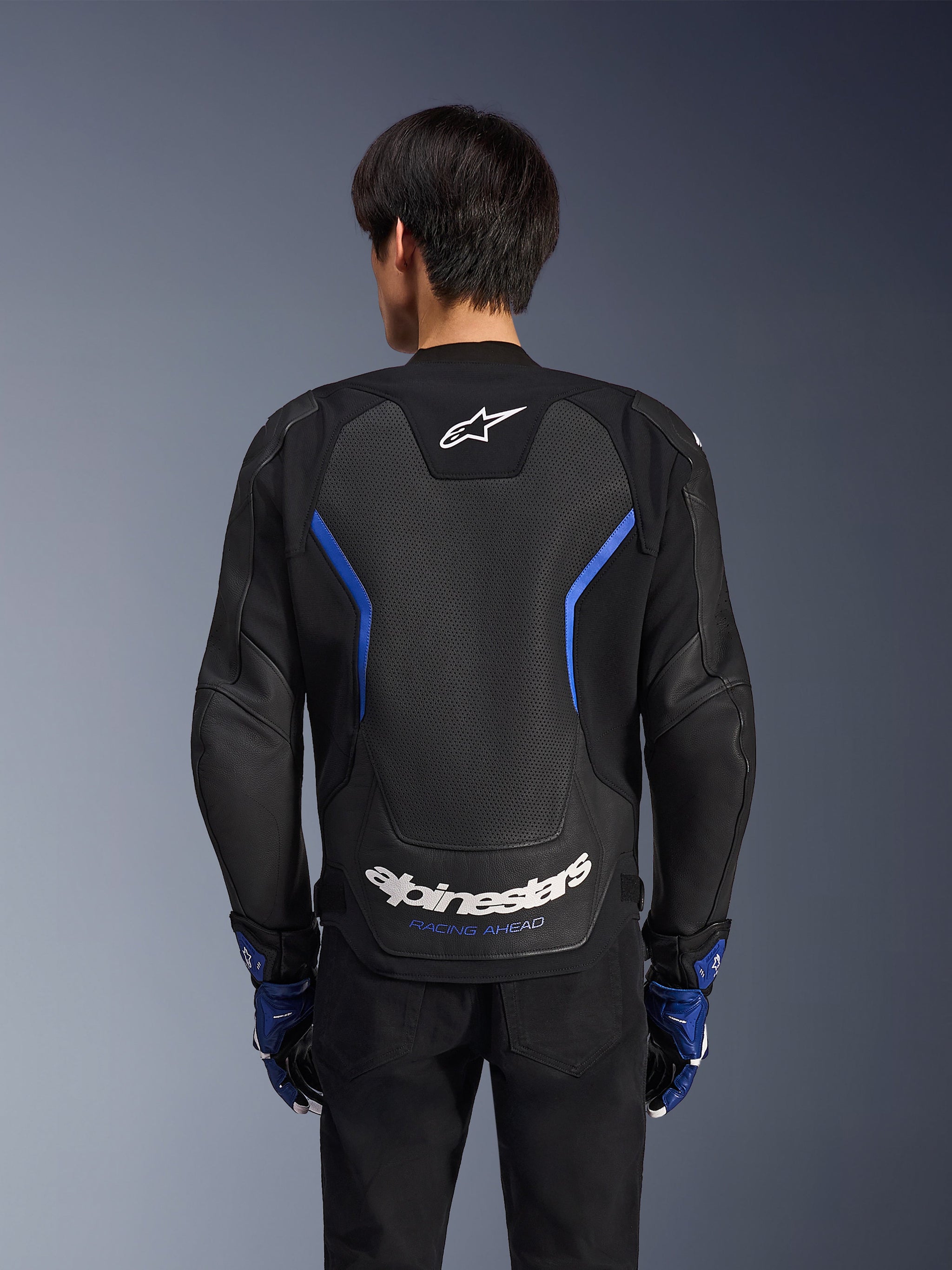 Alpinestars GP Force V2 Airflow Leather Jacket, Black Metallic Blue, back view, featuring a large perforated back panel for ventilation, blue accents, and white Alpinestars branding, worn with matching blue gloves and black pants for sport riding.