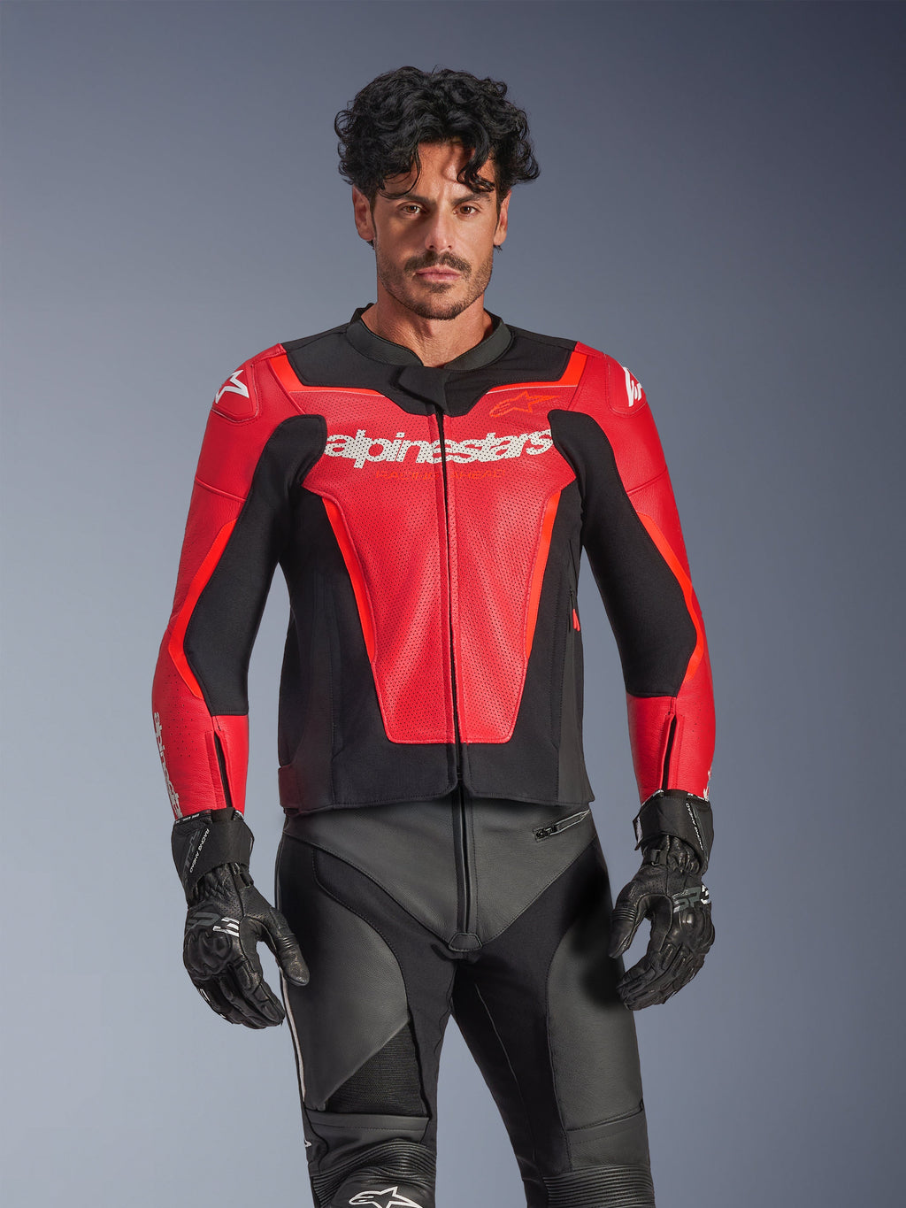 Alpinestars GP Force V2 Air Leather Jacket, Red and Black motorcycle racing jacket, perforated leather construction with white Alpinestars logo, worn by male model and paired with black racing pants and gloves