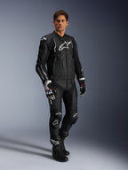 Male rider wearing the Alpinestars Dusk Leather Jacket in Black and White, premium leather jacket with large white branding on the chest, paired with matching leather racing pants, gloves, and boots, complete performance sport riding gear.