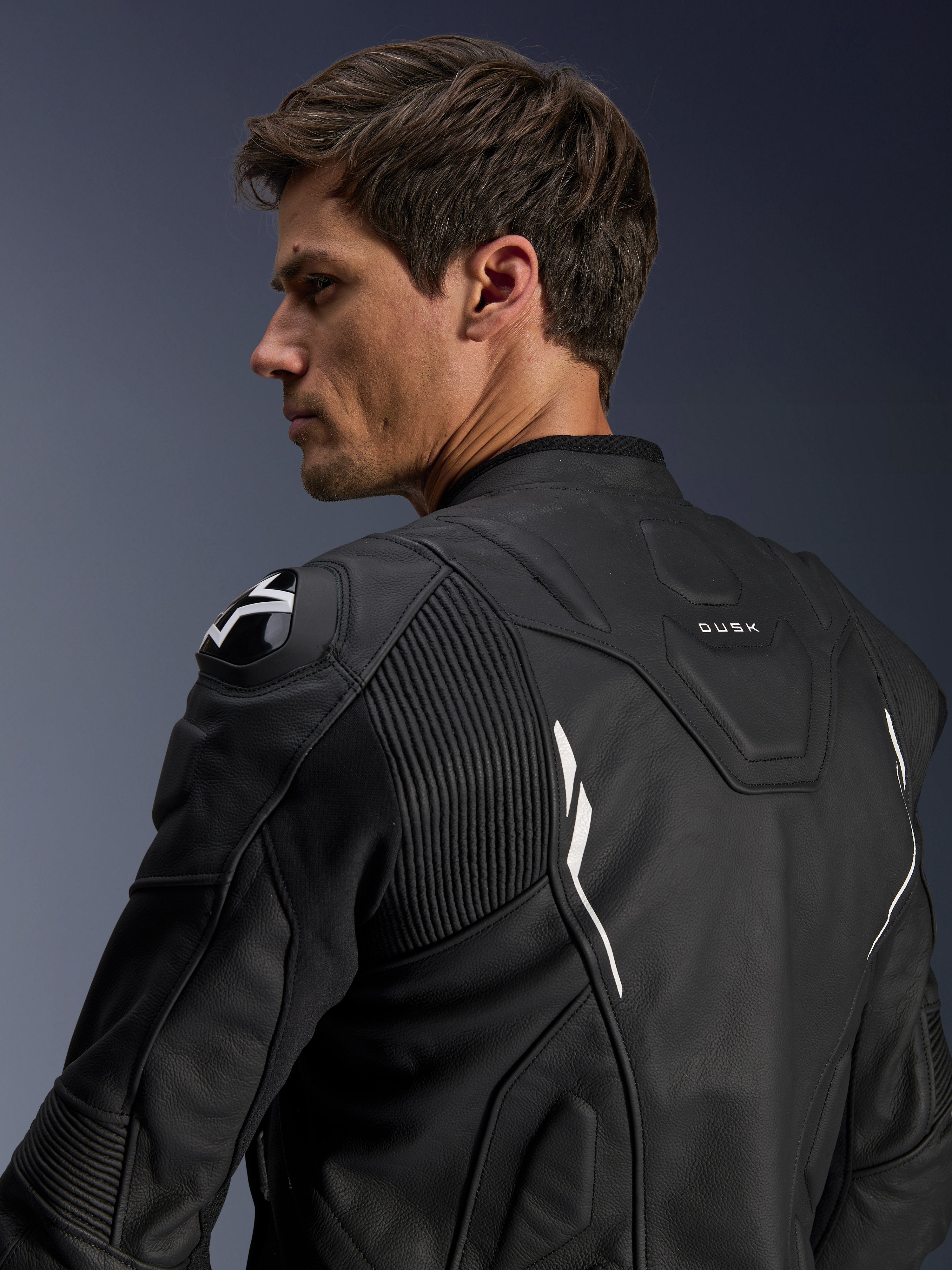 Alpinestars Dusk Leather Jacket, Black with White accents, back view on model, featuring DFS shoulder protectors with Alpinestars logo, accordion leather stretch panels for mobility, and 'DUSK' branding on the upper back, premium bovine leather motorcycle jacket for road and sport riding