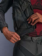 Alpinestars Dusk Leather Jacket, Black, close-up of the waist connection zipper being attached to leather motorcycle pants, worn with a red and black patterned base layer, durable leather construction for road riding.