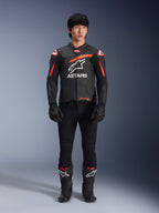 Male model wearing Alpinestars GP Plus R V4 Airflow Leather Jacket, Black with Red Fluo and White accents, large white Astars logo on chest, paired with black technical pants, gloves, and boots, performance motorcycle gear in a studio setting