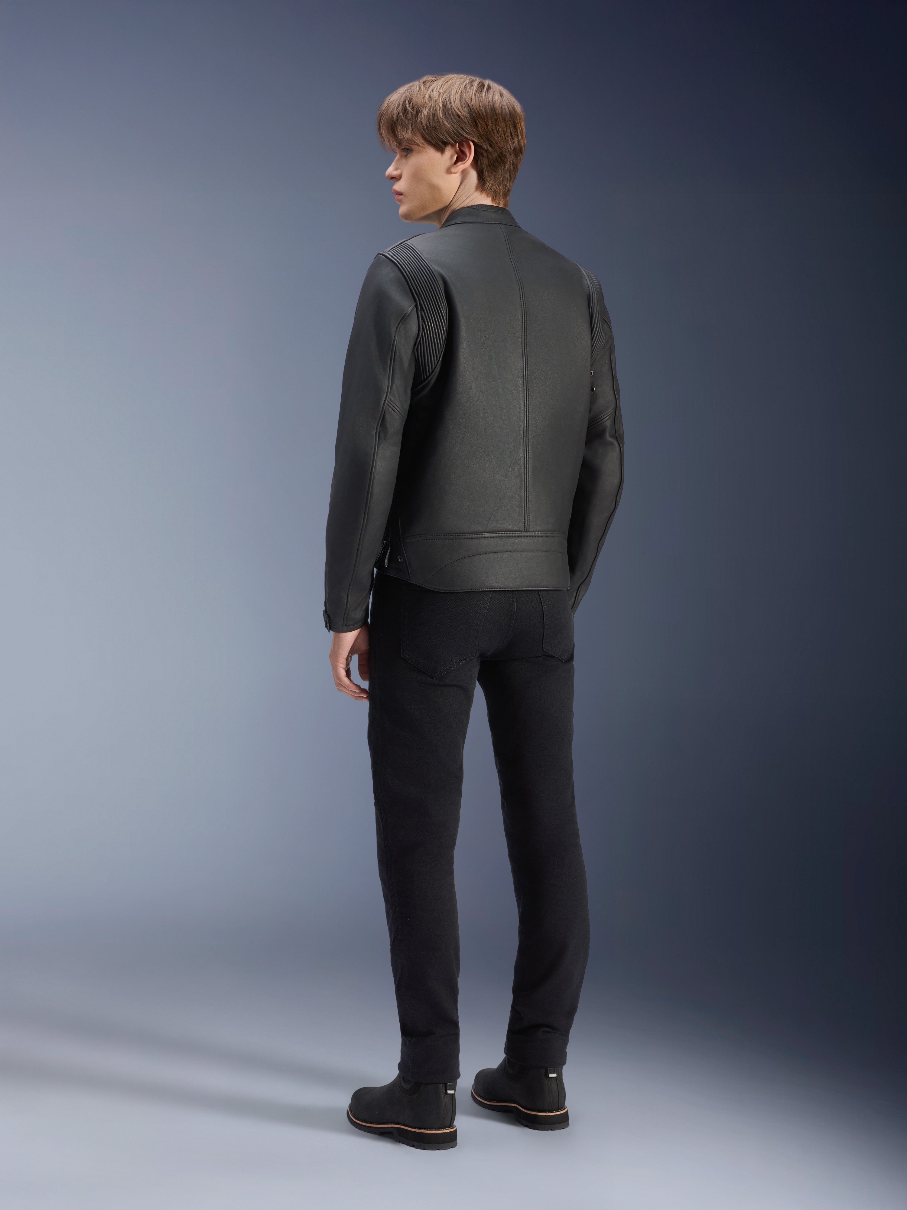Alpinestars Dyno Leather Jacket, Black, worn by a male model from the rear view, featuring ribbed shoulder panels, paired with black pants and boots, heritage-inspired urban motorcycle style.