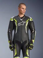 Alpinestars GP Tech V5 One Piece Leather Suit, Black White and Yellow Fluo, professional racing gear, perforated leather with large white Astar logo on chest, fluorescent yellow and white accents, worn with matching racing gloves