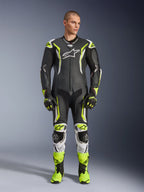 Alpinestars GP Tech V5 One Piece Leather Suit, professional motorcycle racing suit in black and neon yellow fluo with white accents, worn by a model with matching racing gloves and boots, featuring an aerodynamic design and protective sliders.