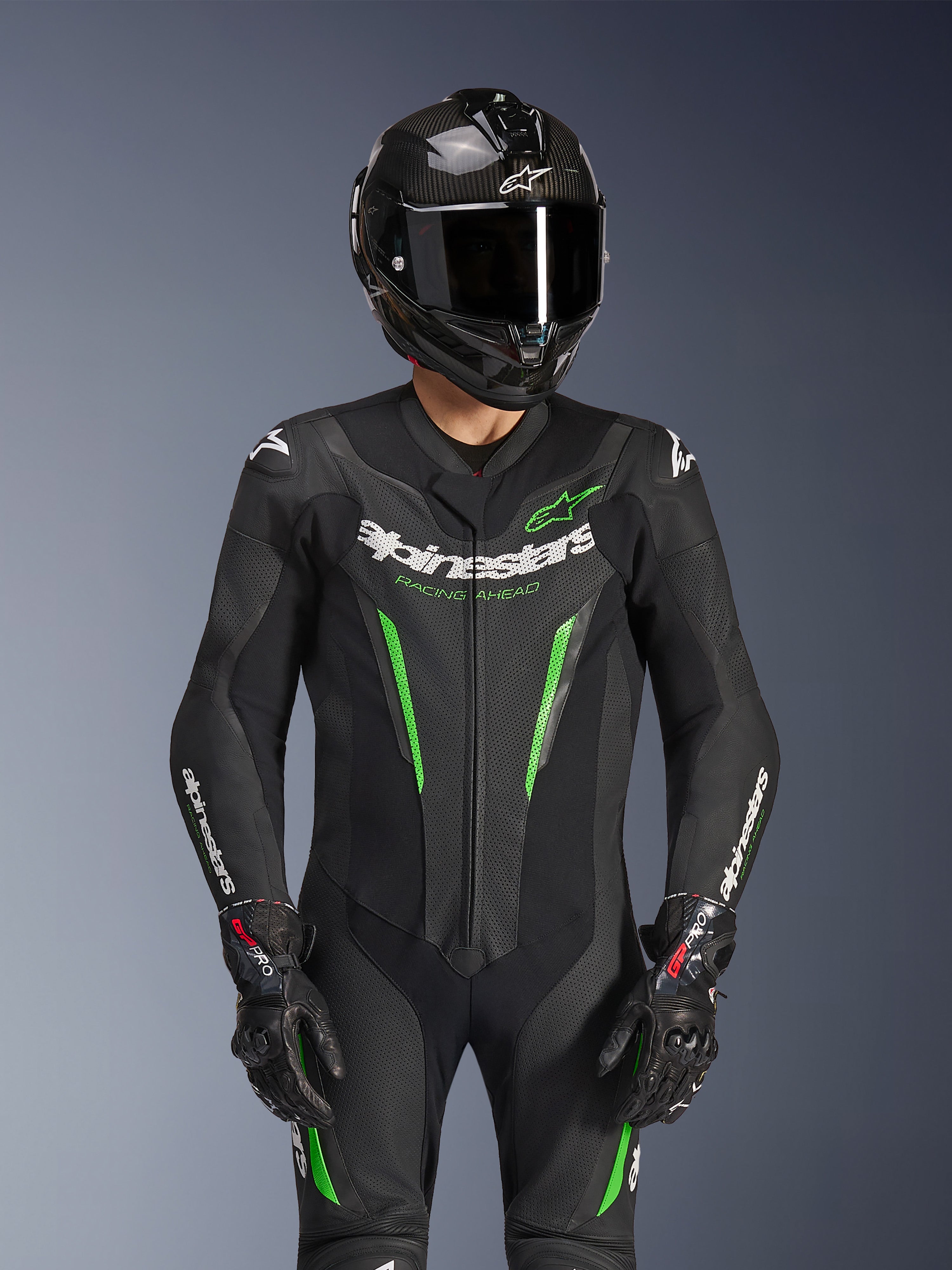 Alpinestars GP Force V2 Leather Suit - 1Piece, Black and Green, motorcycle racing suit worn with a carbon fiber helmet and GP Pro gloves, featuring lime green accents and Alpinestars 'Racing Ahead' branding, engineered for track performance.