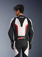 Alpinestars GP Force V2 Leather Suit 1Piece, White Black and Red Fluo, back view on male model, featuring aerodynamic speed hump, perforated leather panels, and Tech-Air Ready logo on the lower back, professional racing gear with black and white gloves