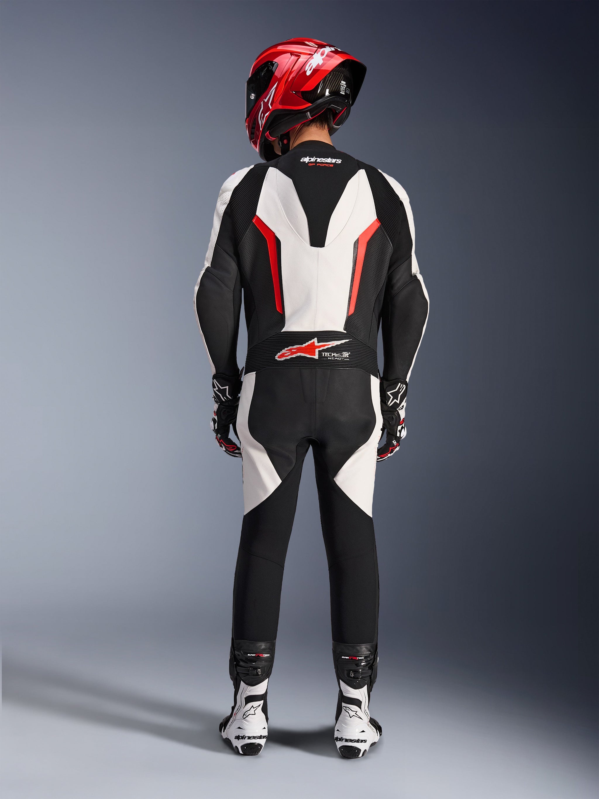 Alpinestars GP Force V2 Leather Suit - 1Piece, White Black Red Fluo, rear view highlighting the aerodynamic speed hump and Tech-Air Ready branding, worn with red racing helmet and white and black boots, track-focused leather suit for performance riding.
