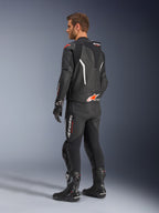 Alpinestars GP Force V2 2-Piece Leather Suit, Black with White and Red Fluo accents, rear three-quarter view on model, featuring an aerodynamic speed hump, perforated leather panels, and bold Alpinestars branding, worn with black racing boots and gloves.