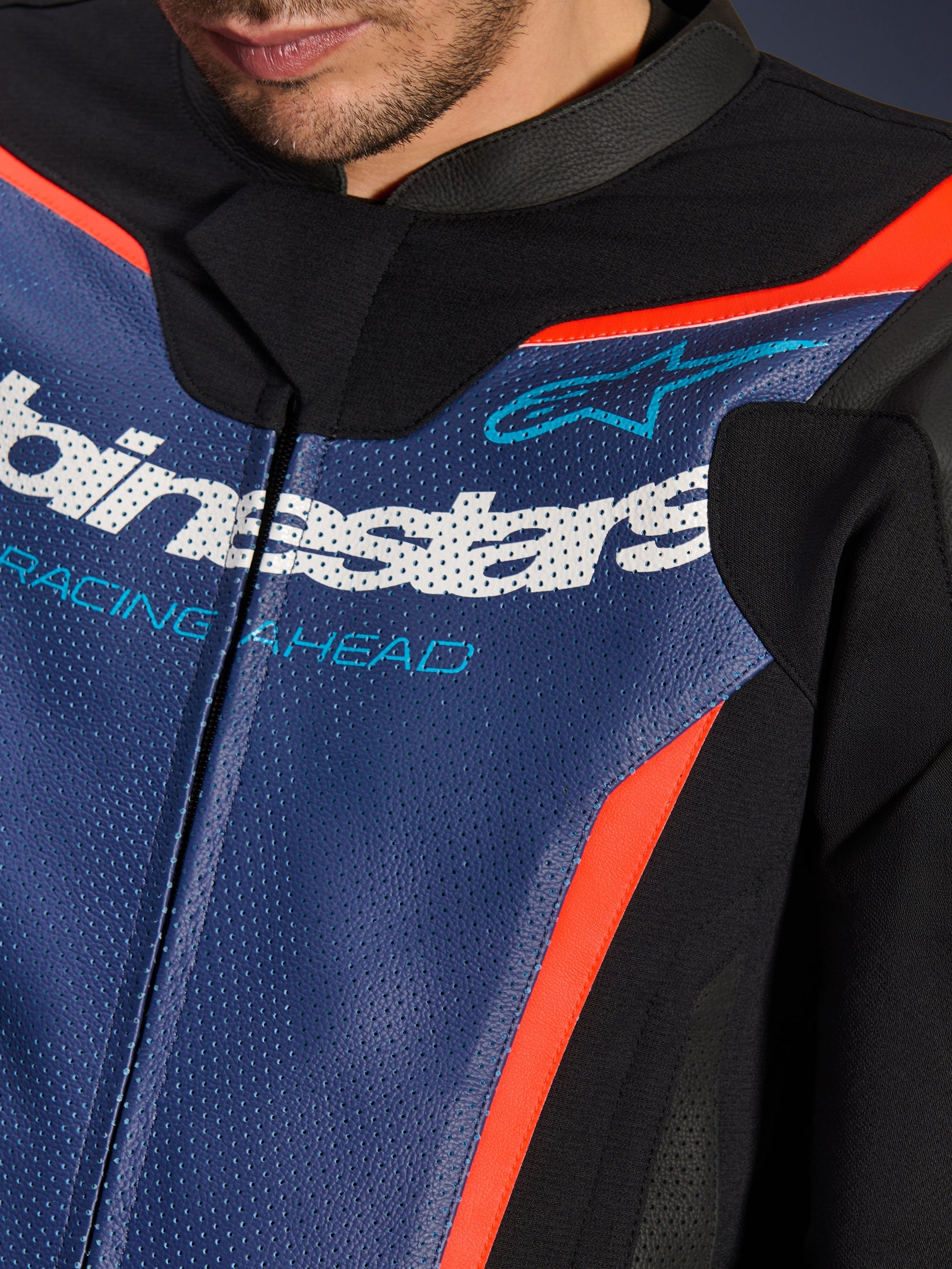 Alpinestars GP Force V2 Leather Suit, 2-Piece, Close-up of chest area, Perforated Blue leather with white logo and 'RACING AHEAD' text, Red Fluo accents and black panels, professional sport riding gear