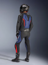Alpinestars GP Force V2 Leather Suit 2-Piece, Black Blue Red Fluo, rear view of rider in professional racing gear, featuring an integrated speed hump and Tech-Air Ready branding, blue and red fluo accents on black leather, worn with a carbon fiber helmet and black boots, high-performance motorcycle apparel