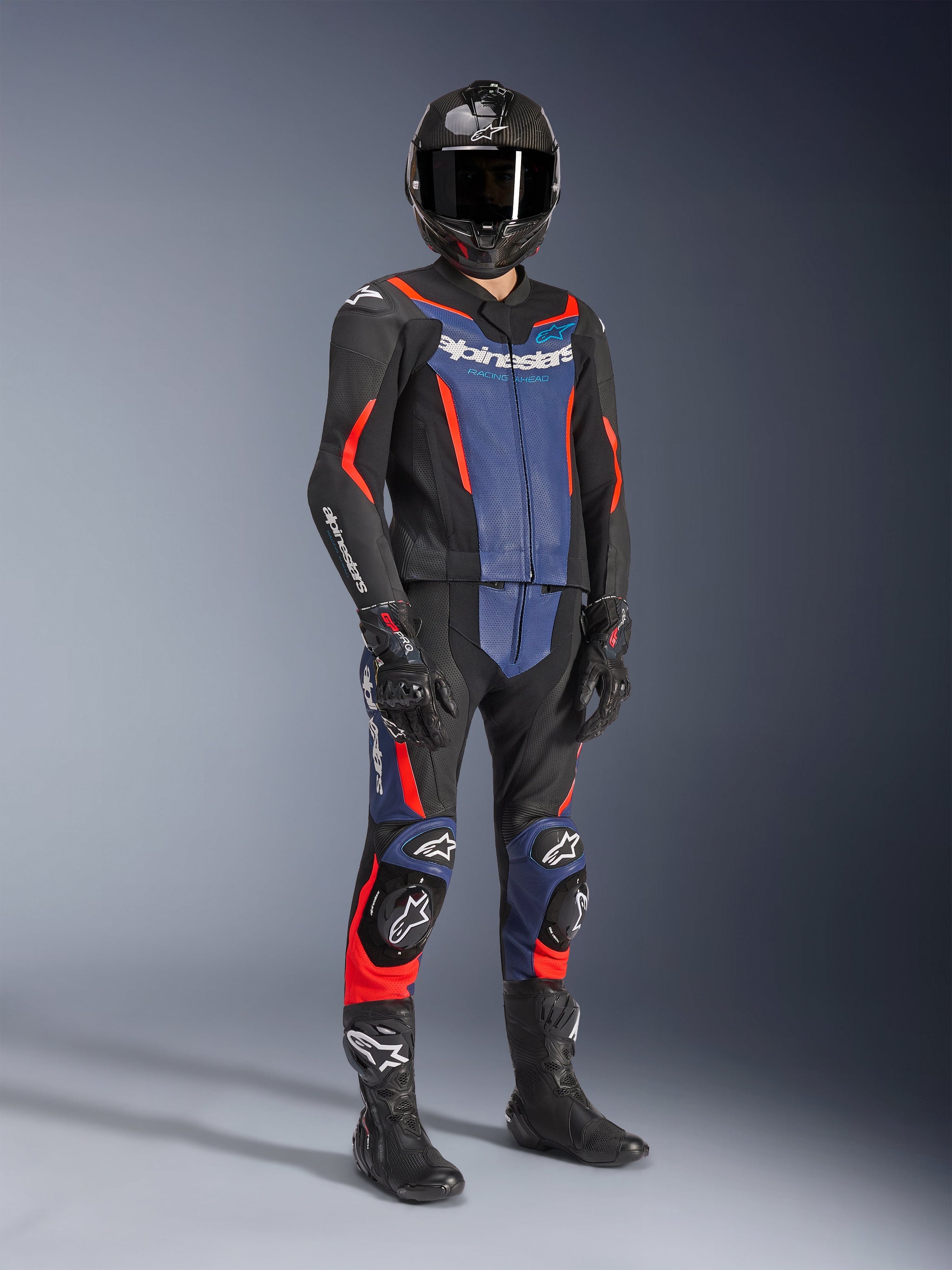 Alpinestars GP Force V2 Leather Suit - 2Piece in Black, Blue, and Red Fluo, worn with a carbon fiber helmet, black racing gloves, and boots, featuring perforated leather panels and white Alpinestars logo, professional sport riding gear.