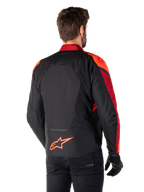 Rear view of a man wearing the Alpinestars T-Jaws V4 Waterproof Jacket in Black Red Fluo Dark Red, featuring vibrant red accents on the shoulders and sleeves, a fluo red Alpinestars logo on the lower back, paired with black pants and gloves.