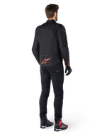Alpinestars T-Jaws V4 Waterproof Jacket, Black and Red Fluo, rear view worn by a male rider, featuring a vibrant red fluo logo on the back, styled with black riding pants and technical boots, sport motorcycle apparel.