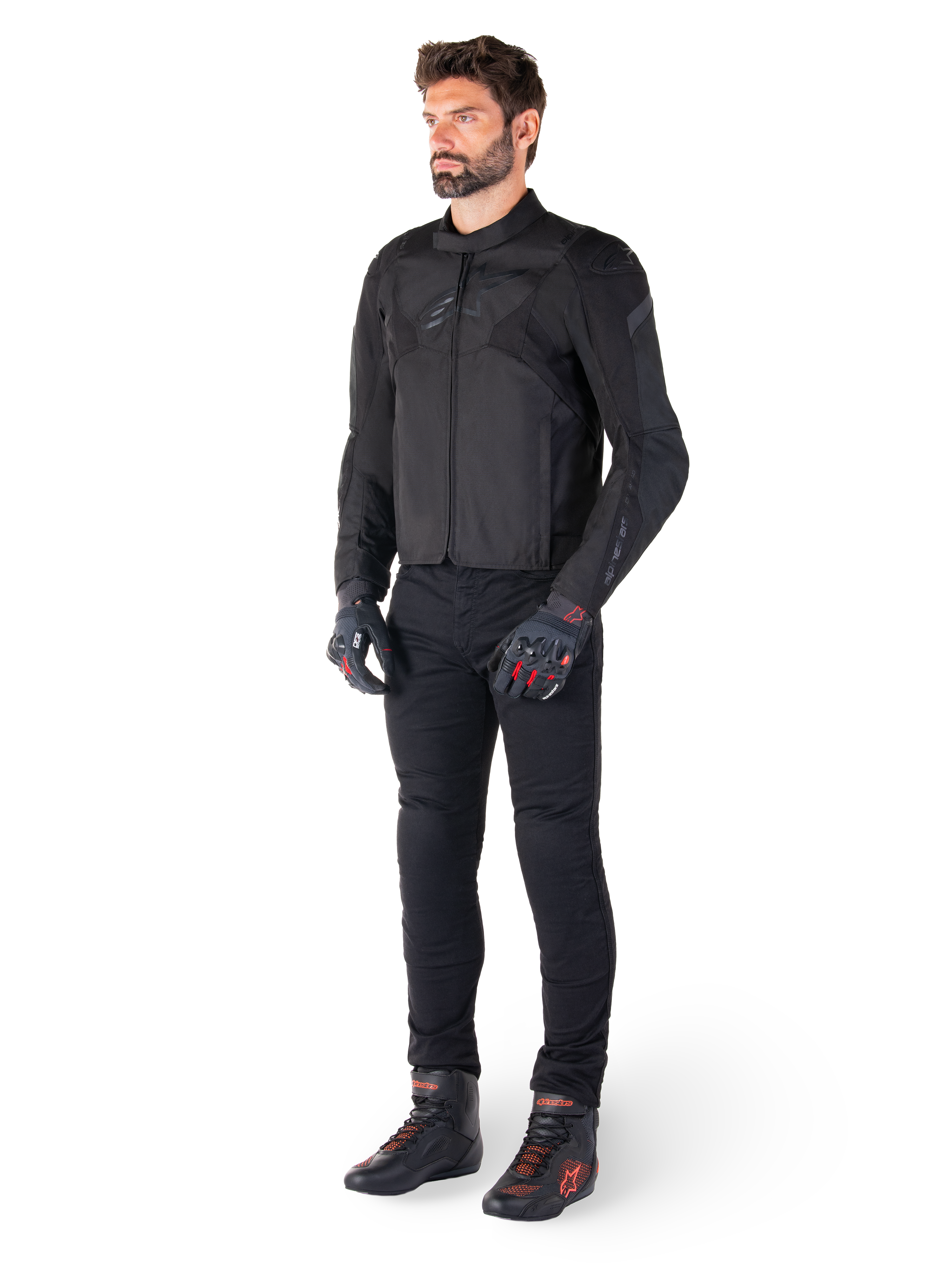 Male model wearing the Alpinestars T-Jaws V4 Waterproof Jacket in Black, paired with black riding pants, black gloves with red accents, and black motorcycle shoes, featuring a sleek sport fit and subtle branding, isolated on a white background.