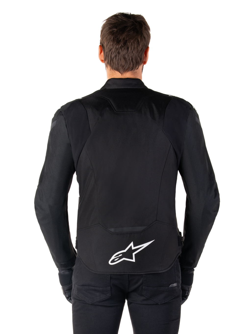 Alpinestars T-Jaws V4 Waterproof Jacket, Black motorcycle jacket seen from the back, featuring a white Alpinestars logo on the lower back, extended rear for coverage, worn by model with black pants and gloves, sleek sport textile design