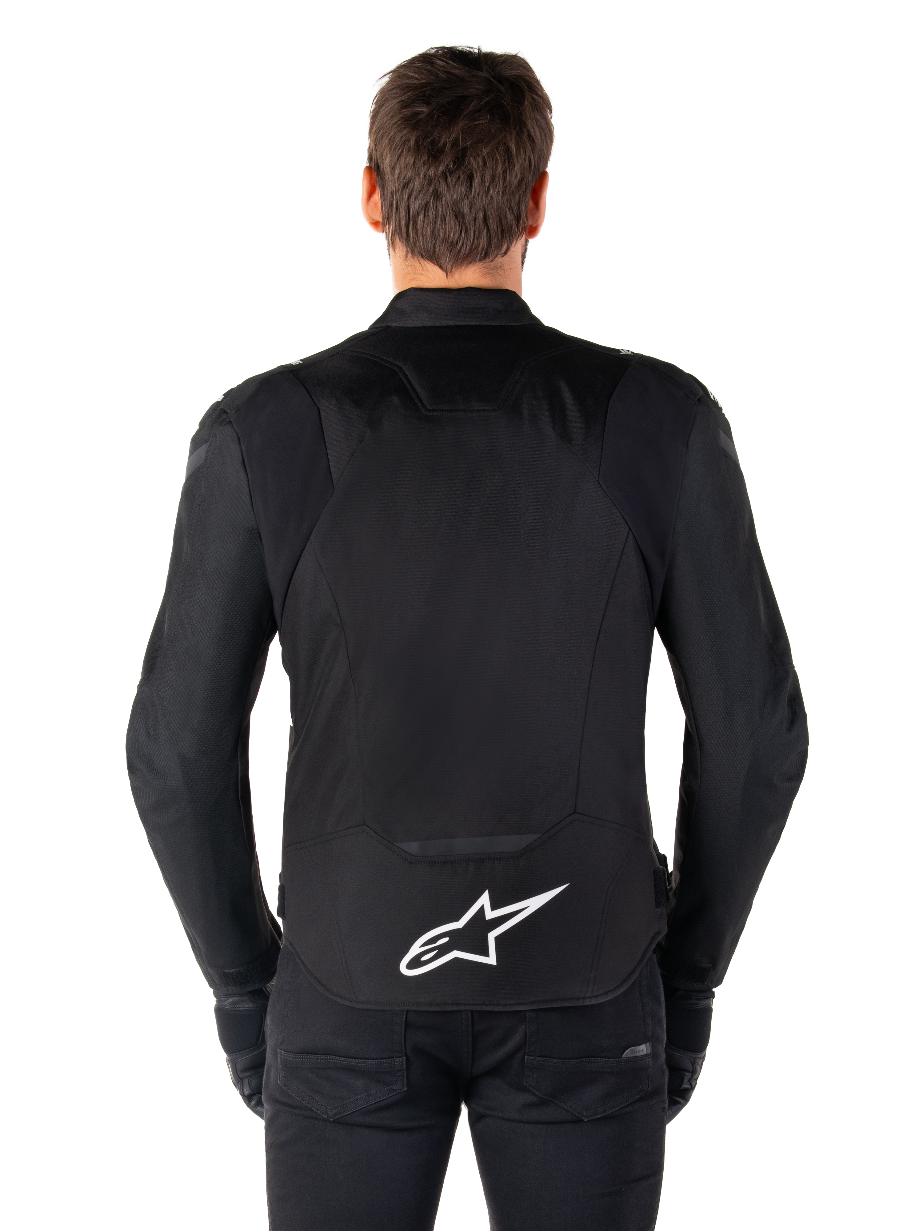 Alpinestars T-Jaws V4 Waterproof Jacket, Black motorcycle jacket seen from the back, featuring a white Alpinestars logo on the lower back, extended rear for coverage, worn by model with black pants and gloves, sleek sport textile design