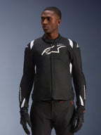 Alpinestars T-SP 1 V2 Waterproof Jacket, Sport Textile Motorcycle Jacket, Black and White with subtle red details, worn by a male model with matching gloves and pants, featuring white Alpinestars logo on chest, T-SP-1 branding, and protective silhouette for road riding
