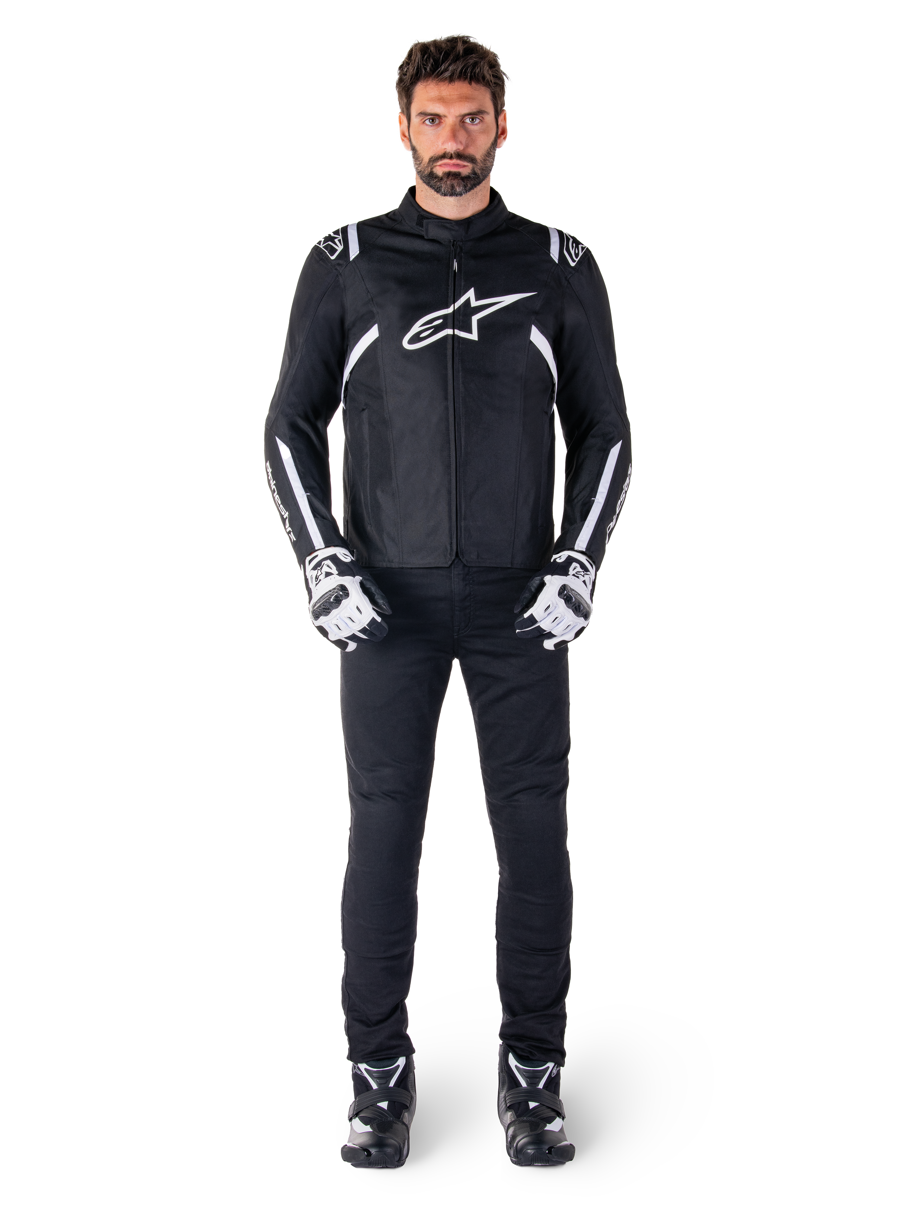 Alpinestars T-SPS V2 Waterproof Jacket, Black and White, worn by male model with black pants and matching gloves, featuring white Alpinestars logo on chest and accents on sleeves, sport-cut silhouette for all-weather motorcycle riding