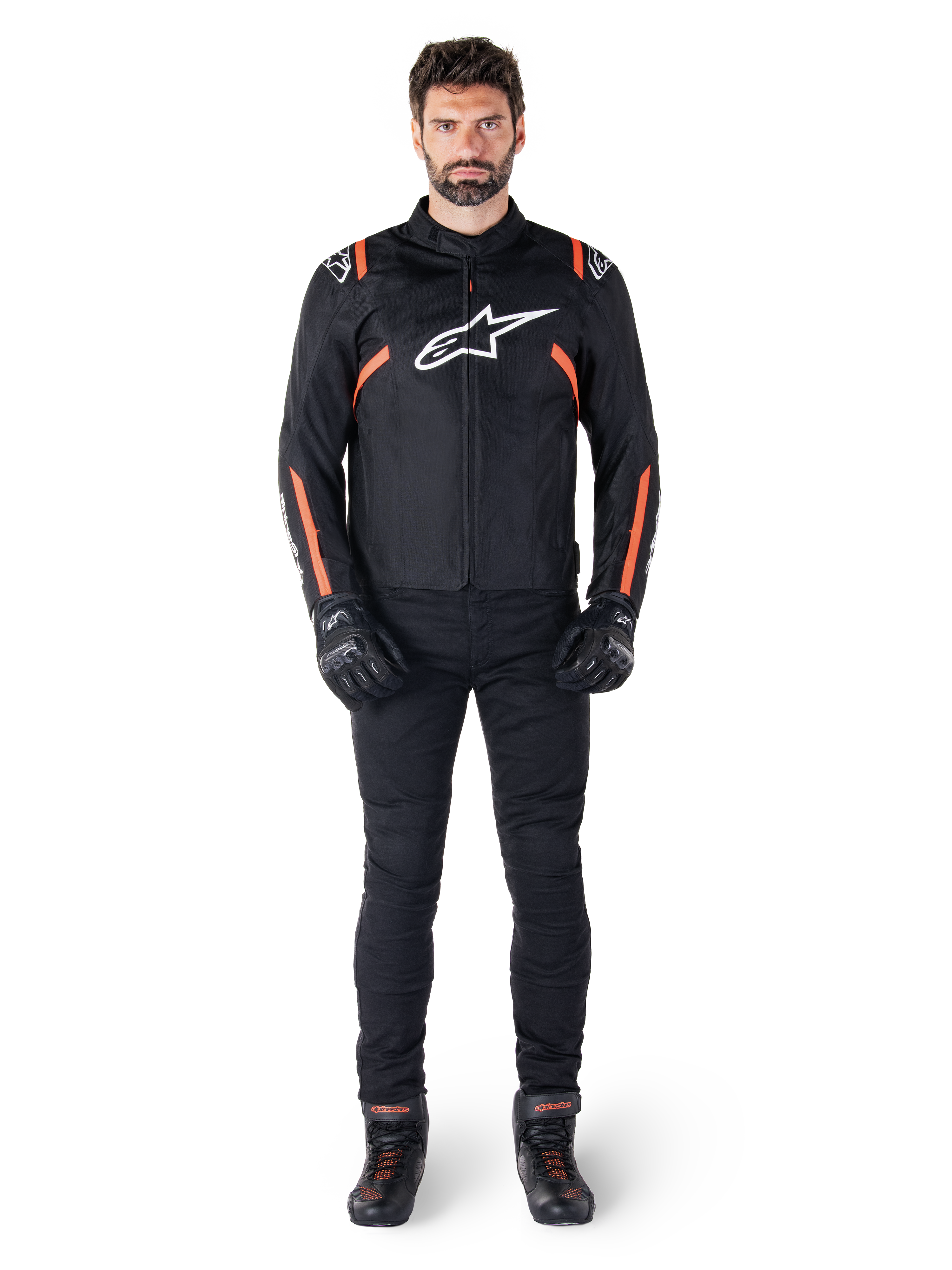Male model wearing the Alpinestars T-SPS V2 Waterproof Jacket in Black White Red Fluo, paired with black motorcycle pants and gloves, featuring a white Alpinestars logo on the chest and red accents on the sleeves.