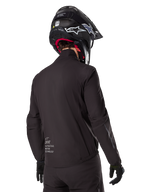 Alpinestars AMT-8 Stretch Drystar® XF Liner, Black Waterproof Jacket Liner, rear view on a rider wearing a black helmet and gloves, featuring Alpinestars Motion Technology branding on the lower back, minimalist and functional design for adventure riding.