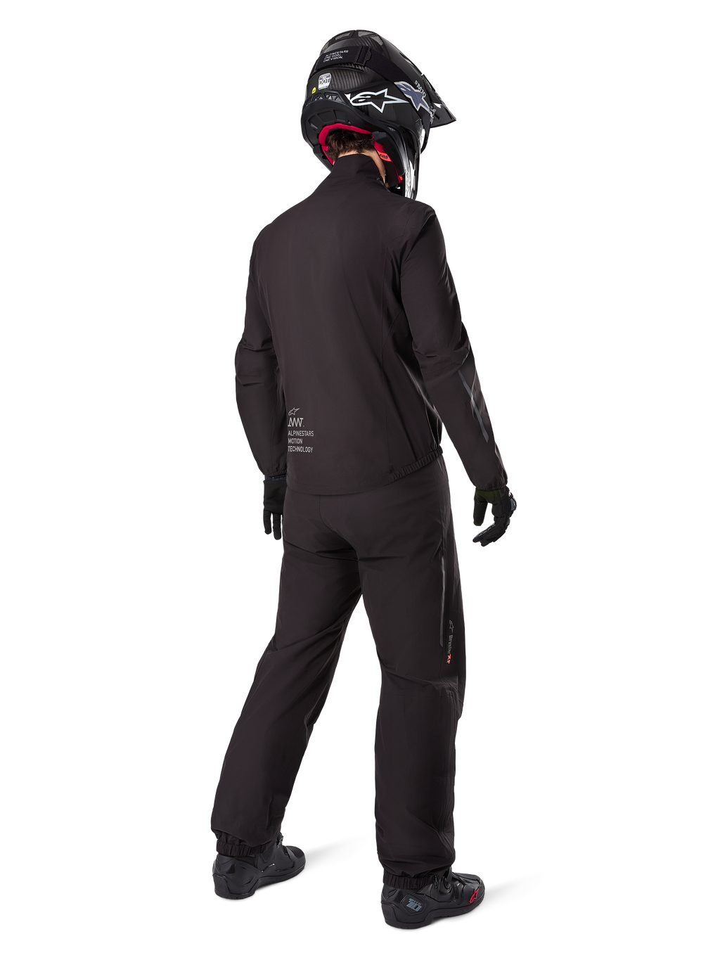 Rear view of a rider wearing the Alpinestars AMT-8 Stretch Drystar® XF Jacket liner, Black technical motorcycle gear, worn with matching pants and black helmet, featuring "AMT Alpinestars Motion Technology" branding on the back, sleek minimalist design for adventure touring