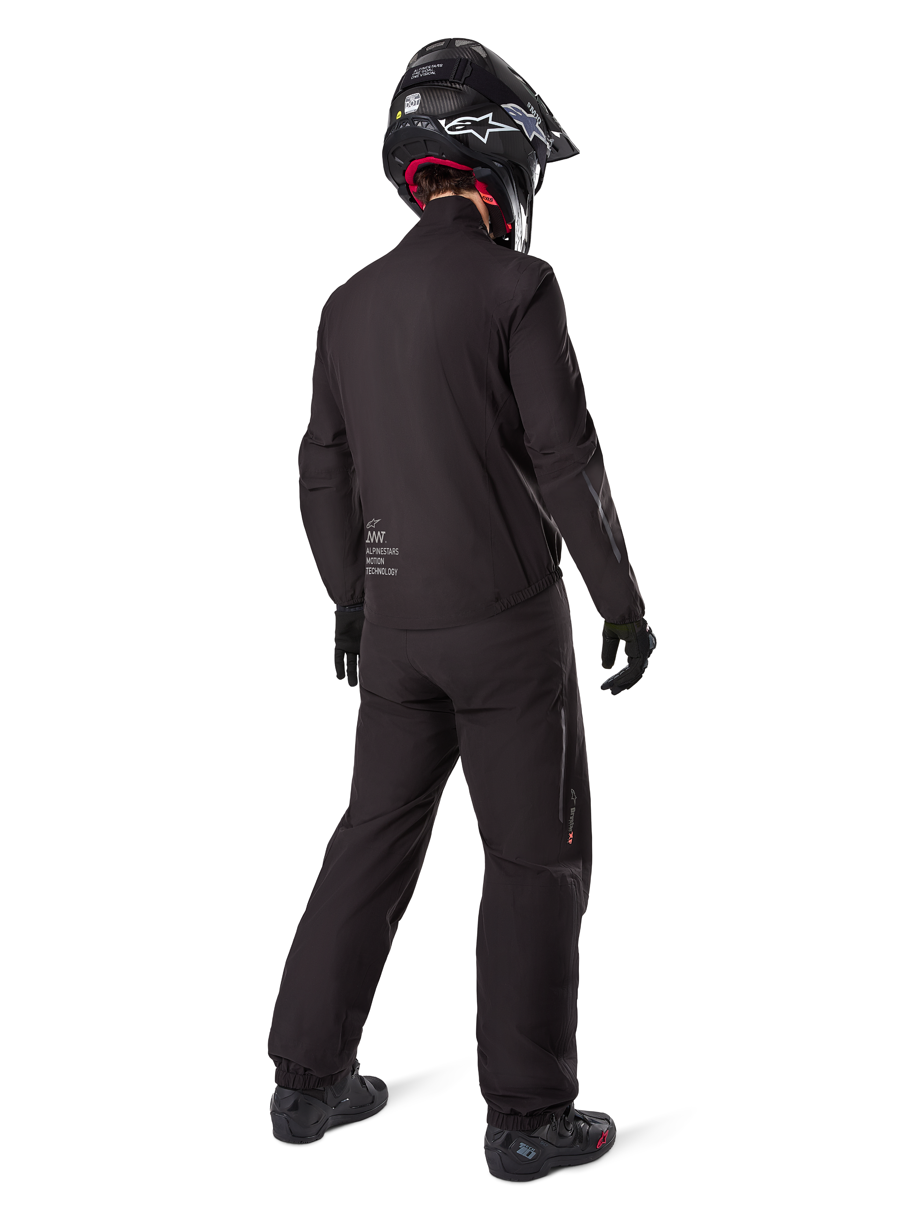 Rear view of a rider wearing the Alpinestars AMT-8 Stretch Drystar® XF Jacket liner, Black technical motorcycle gear, worn with matching pants and black helmet, featuring "AMT Alpinestars Motion Technology" branding on the back, sleek minimalist design for adventure touring
