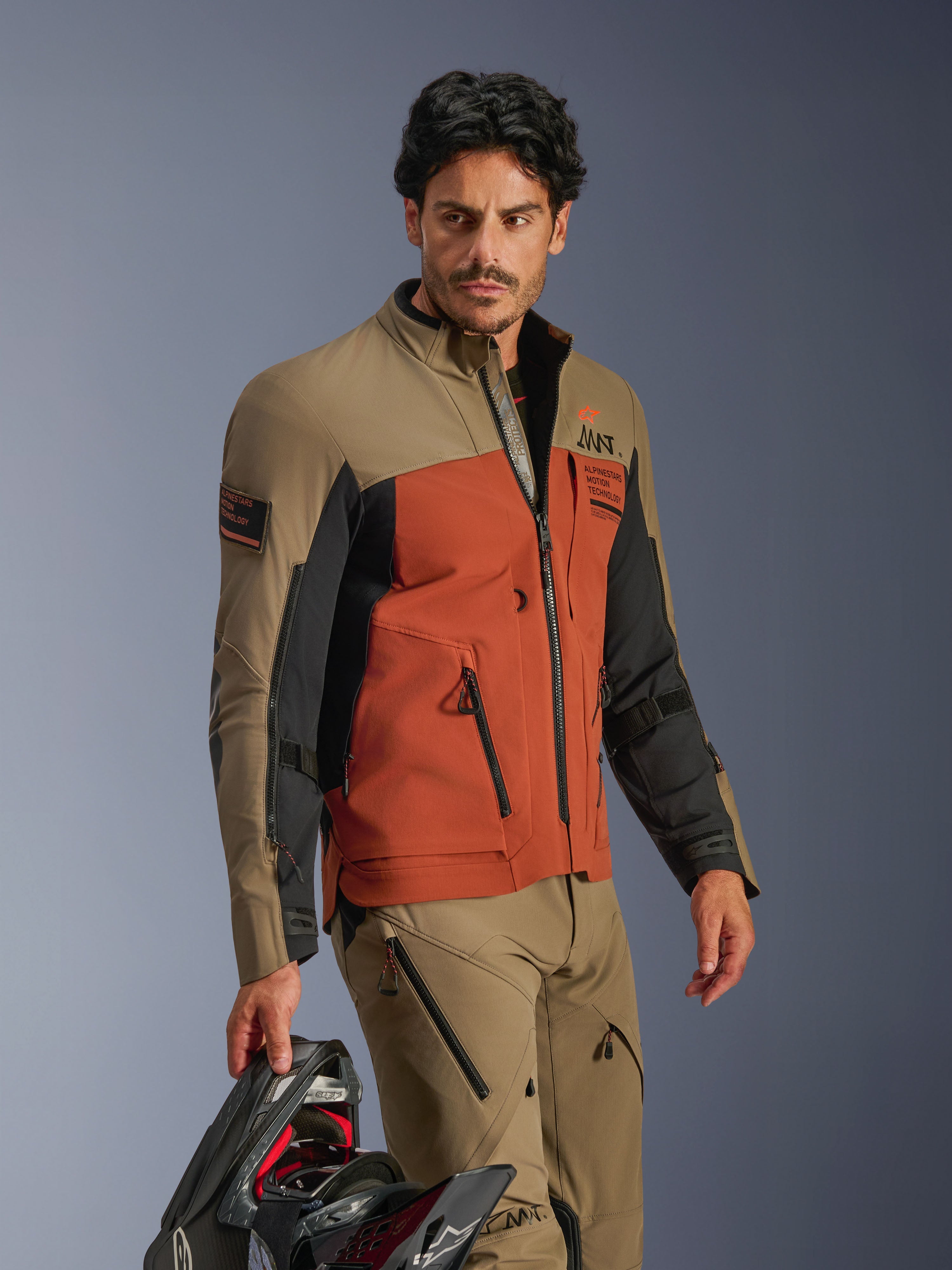 Alpinestars AMT-8 Stretch Drystar® XF Jacket, Walnut Rust Black, adventure motorcycle jacket with high-performance stretch material, worn with matching walnut pants and holding a black helmet, adventure touring gear for long-range riding