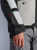 Alpinestars Andes V4 Drystar® Jacket, adventure motorcycle jacket, Ice Gray and Black panels, close-up of sleeve featuring red Drystar® logo and adjustable straps, functional textile design for all-weather riding