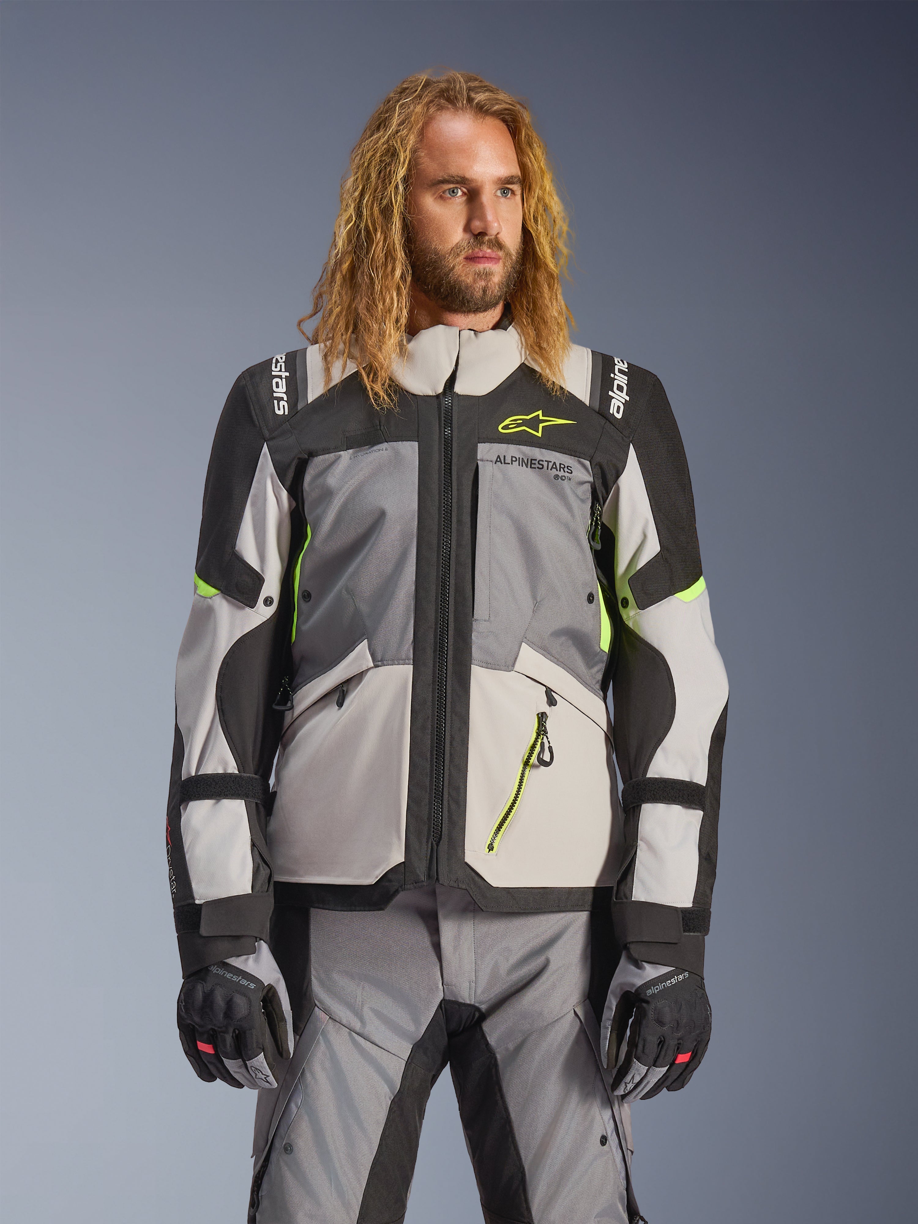 Alpinestars Andes V4 Drystar Jacket, Adventure Touring Motorcycle Jacket, Dark Gray and Ice Gray with Neon Yellow accents, worn by a model with matching pants and gloves, multi-pocket textile design for all-weather riding