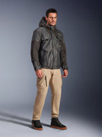 Male model wearing the Alpinestars Mospher Waterproof Jacket in Black, utility-inspired waterproof parka with a multi-pocket design and hood, paired with tan cargo pants and black high-top sneakers, urban motorcycle commuter gear.