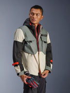 Alpinestars Mospher Waterproof Jacket in Fur Gray Black Ice, multi-panel textile parka with gray, black, and off-white sections, featuring bright red zipper and strap accents, tactical-inspired design with hood and utility pockets, worn by a model holding motorcycle gloves.