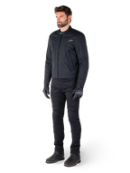 Male rider wearing the Alpinestars Clayton WR Jacket, Black urban motorcycle jacket, slim-fit design with quilted shoulder accents and matte finish, paired with black technical riding pants and gloves.