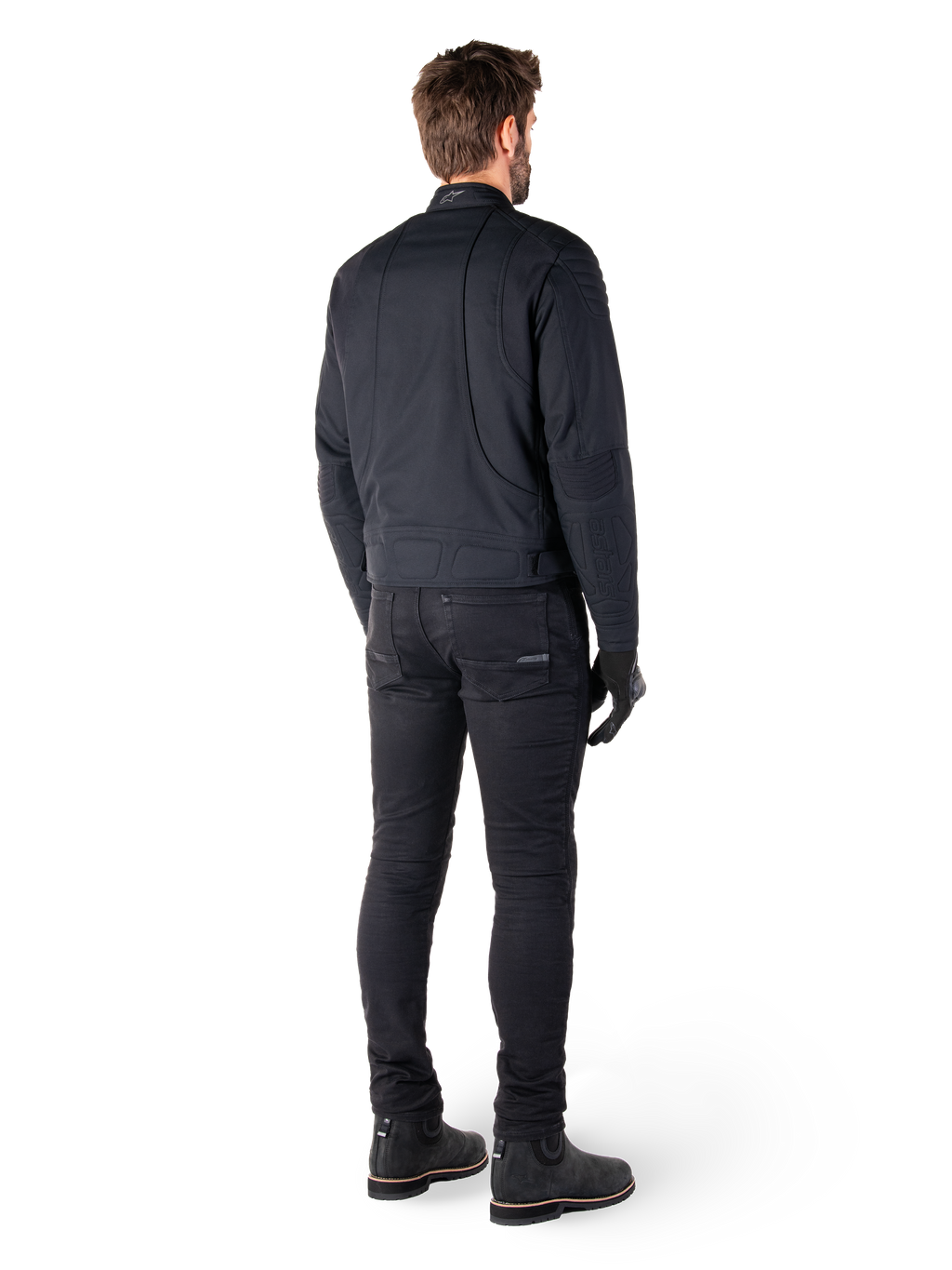 Rear view of a rider wearing the Alpinestars Clayton WR Jacket in Black, featuring quilted elbow and shoulder panels, ergonomic curved stitching, and reflective collar detailing, paired with black riding pants and boots for an urban motorcycle look.