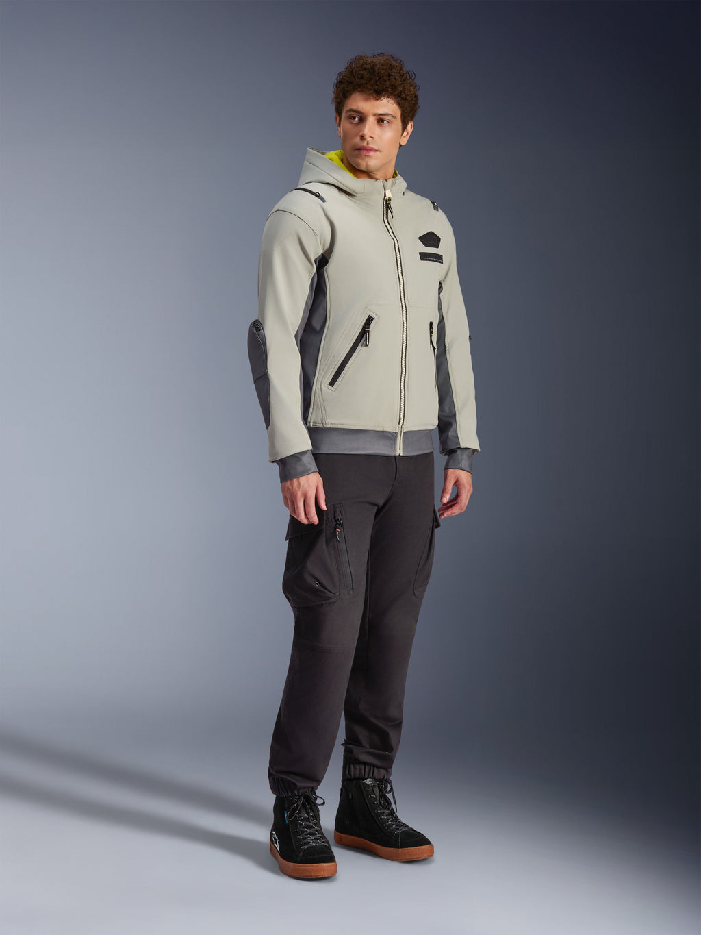 Alpinestars Moblast Waterproof Jacket, Iron Gray and Dark Sage, urban motorcycle riding jacket with a hoodie design, worn by a model with dark riding pants and black boots, minimalist cyber-tech aesthetic with a yellow interior hood and waterproof zippers