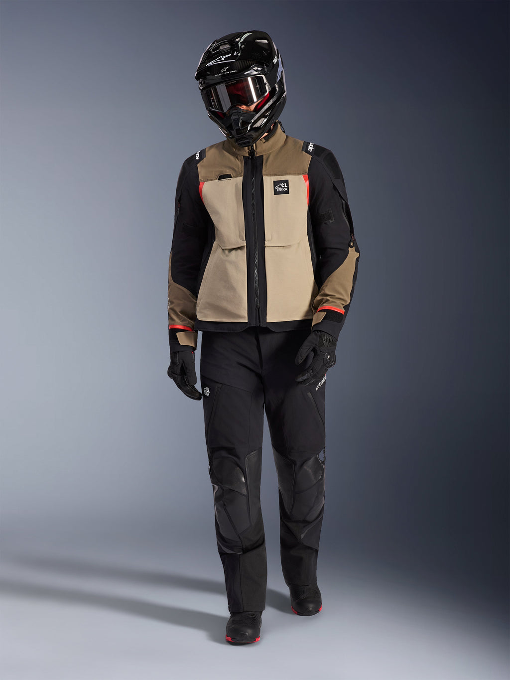 Alpinestars Andes Pro Drystar® XF Jacket in Walnut Aluminum, worn with black adventure pants, black gloves, and a black full-face helmet with goggles, featuring red highlights and All Terra branding, professional adventure touring setup
