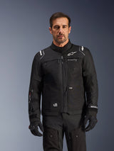 Alpinestars Cusco Drystar® Jacket, Black motorcycle jacket, worn by a model with matching black gloves and pants, featuring technical textile construction with white Alpinestars logos, designed for road adventure touring
