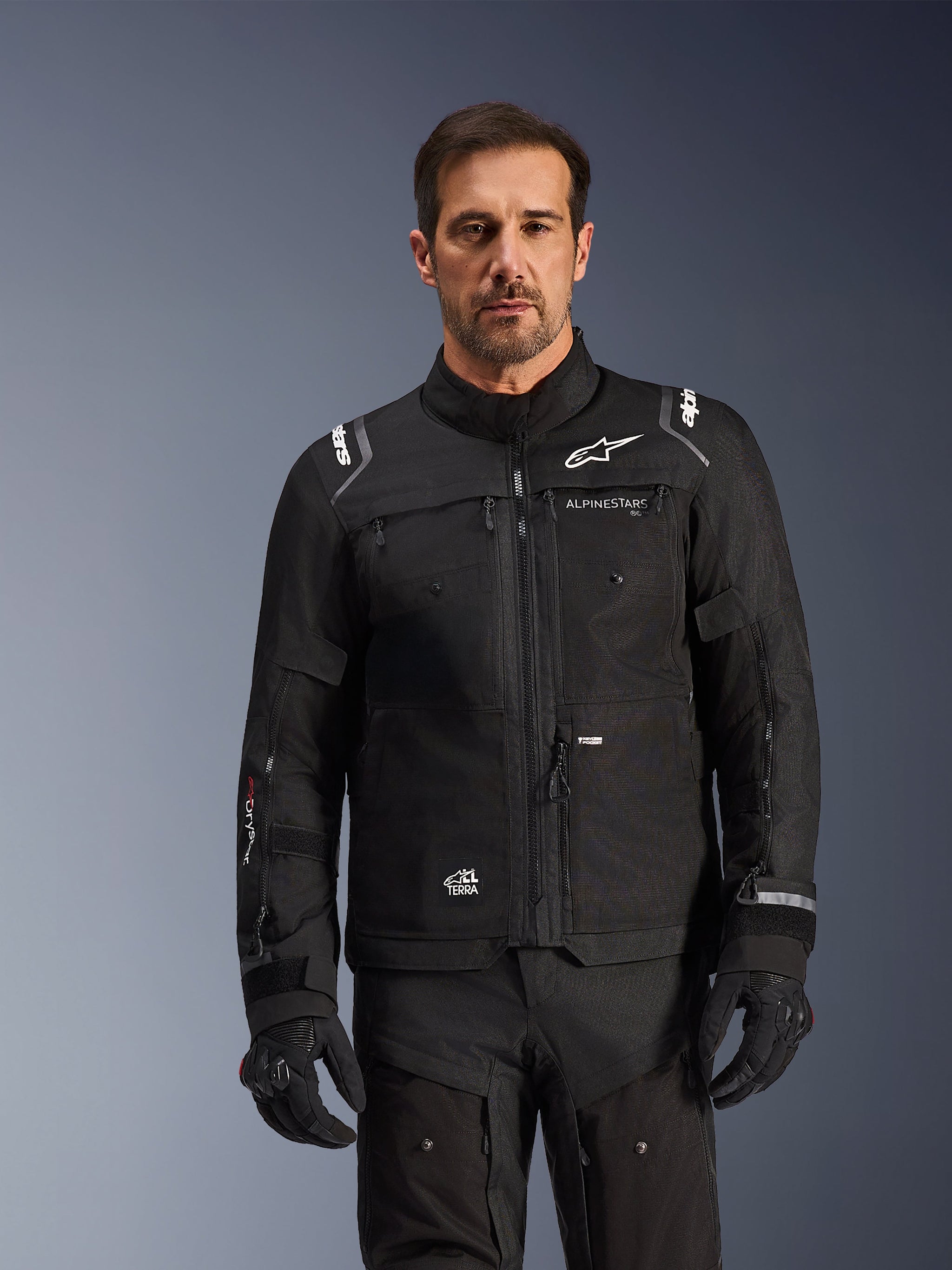 Alpinestars Cusco Drystar® Jacket, Black motorcycle jacket, worn by a model with matching black gloves and pants, featuring technical textile construction with white Alpinestars logos, designed for road adventure touring