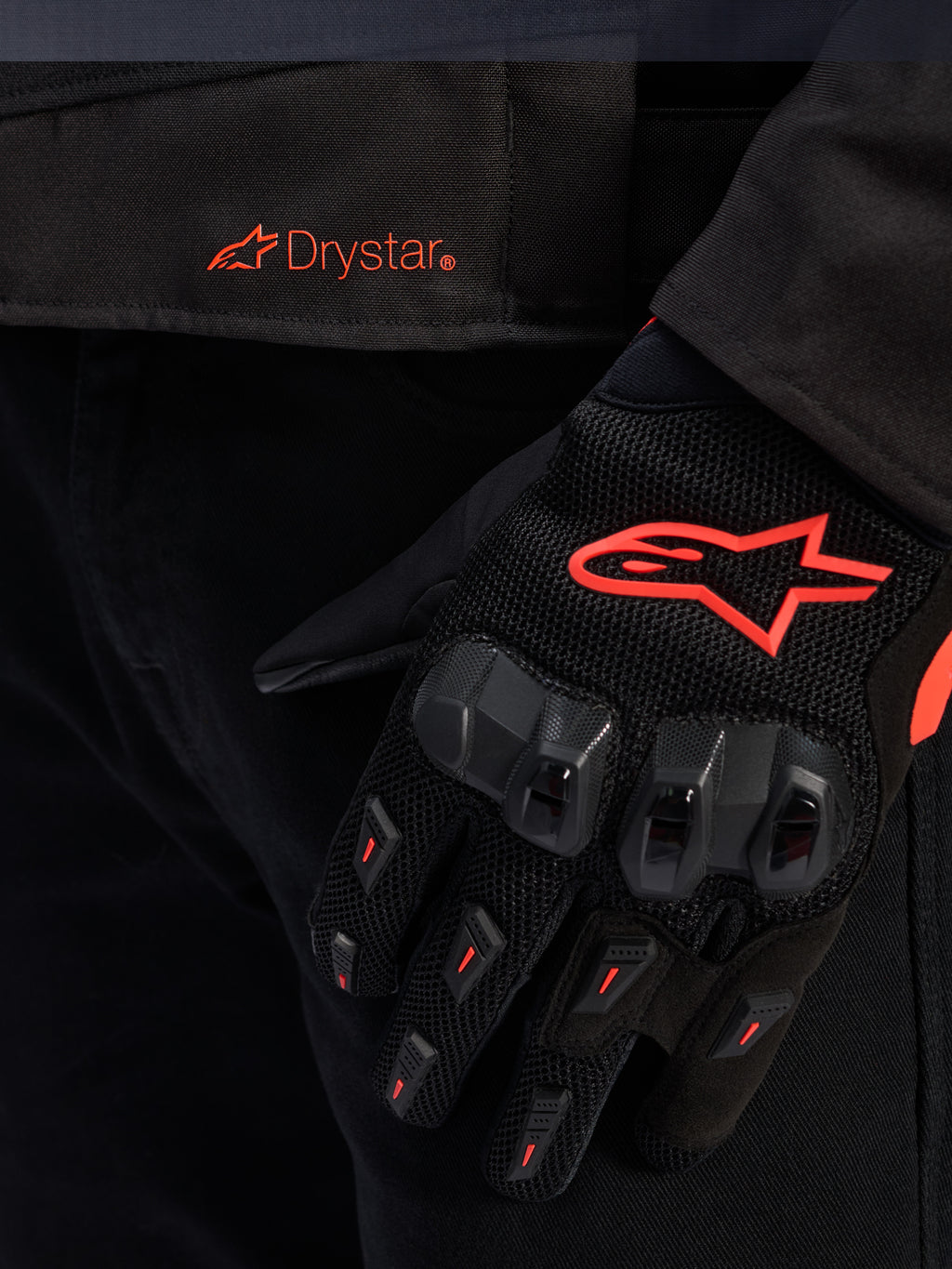 Close-up of the Alpinestars T-GP R V3 Drystar® Jacket waist featuring a red Drystar logo, shown with a black motorcycle glove with a red Alpinestars star logo, mesh fabric, and reinforced knuckle protection.