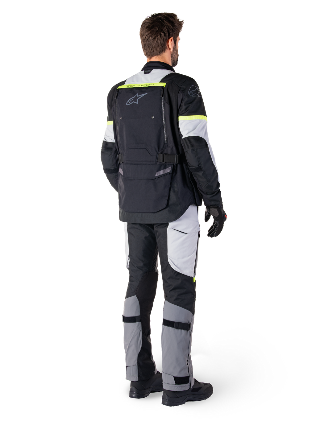 Rear view of a rider wearing the Alpinestars Bogotá Pro Drystar® Jacket in Black Ice Gray Yellow Fluo, paired with matching adventure touring pants, featuring a large back pocket and yellow fluorescent accents, all-season textile motorcycle gear.