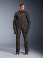 Female rider wearing Alpinestars Stella Andes V4 Drystar® Jacket in Black, paired with matching black adventure-touring pants and gloves, featuring technical textile construction with multiple utility pockets and white Alpinestars branding, complete all-weather motorcycle gear