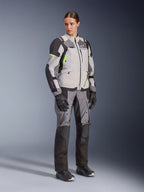 Woman wearing Alpinestars Stella Andes V4 Drystar® Jacket and matching pants, Ice Gray and Dark Gray with Yellow Fluo accents, complete adventure touring gear set with black gloves and boots, full-length studio shot.