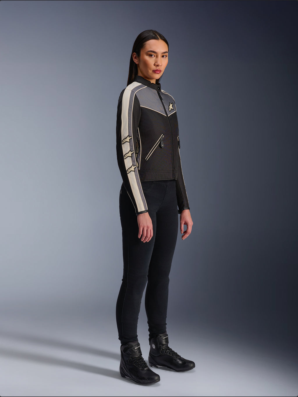 Alpinestars Stella T-Dyno WR Jacket, Women's textile motorcycle jacket, Black, Dark Gray, and Ecru, featuring vintage-inspired design with cream sleeve stripes and star logos, worn with black pants and riding boots, heritage-inspired urban riding gear