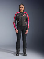Woman wearing Alpinestars Stella T-Dyno WR Jacket, Black with Bright Red and Fuchsia accents, vintage-style textile jacket with pink logo and sleeve stripes, worn with black pants and lace-up boots, urban motorcycle gear