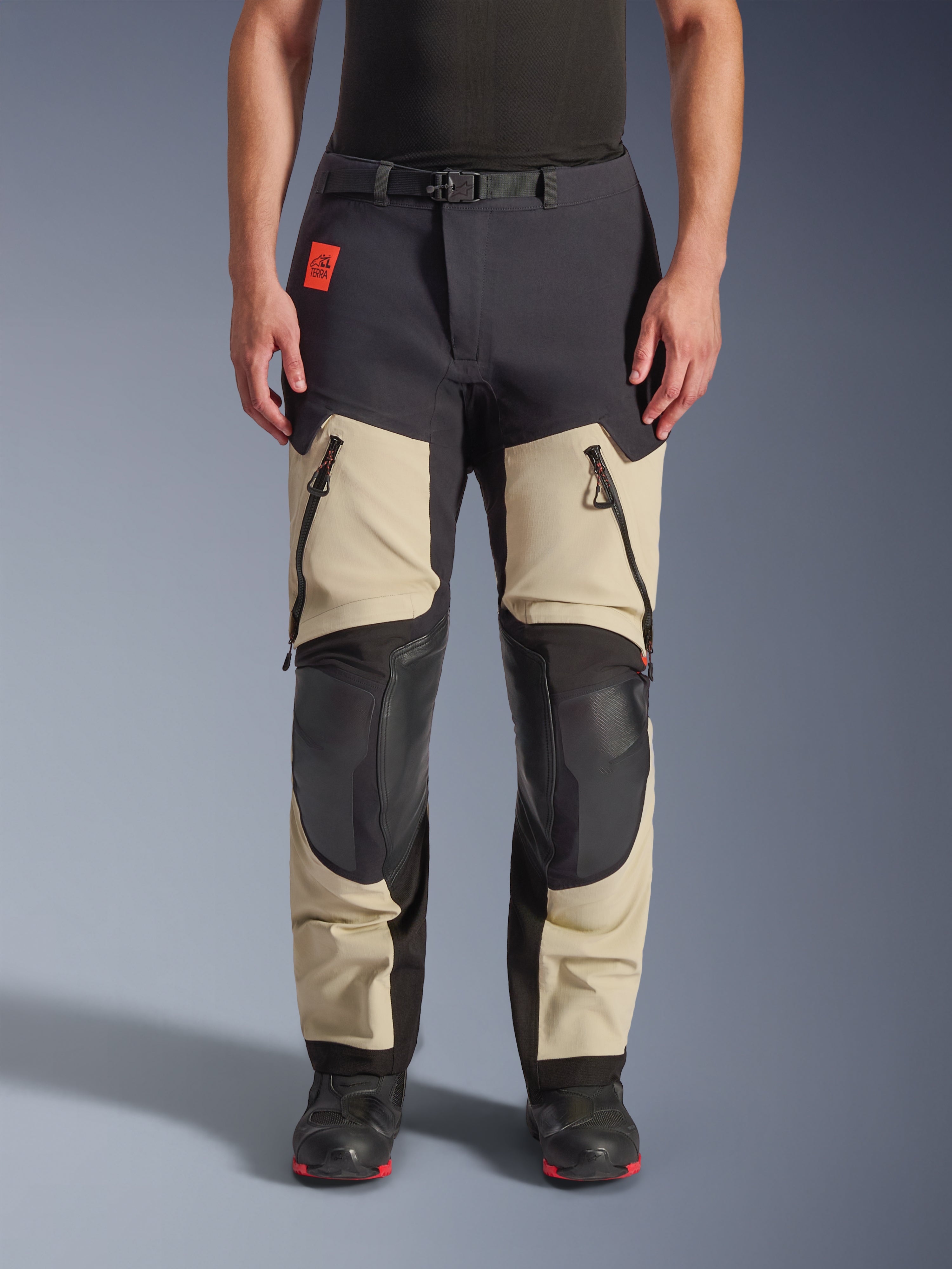 Alpinestars Halo Pro Drystar® XF Laminated Pants, Adventure Motorcycle Pants, Mastic Black, front view worn by a rider, featuring large zippered thigh vents, reinforced black knee panels, and tan textile construction, paired with black and red riding boots